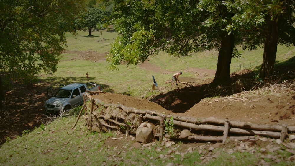 The berm and its log wall from above, a pickup parked under the trees