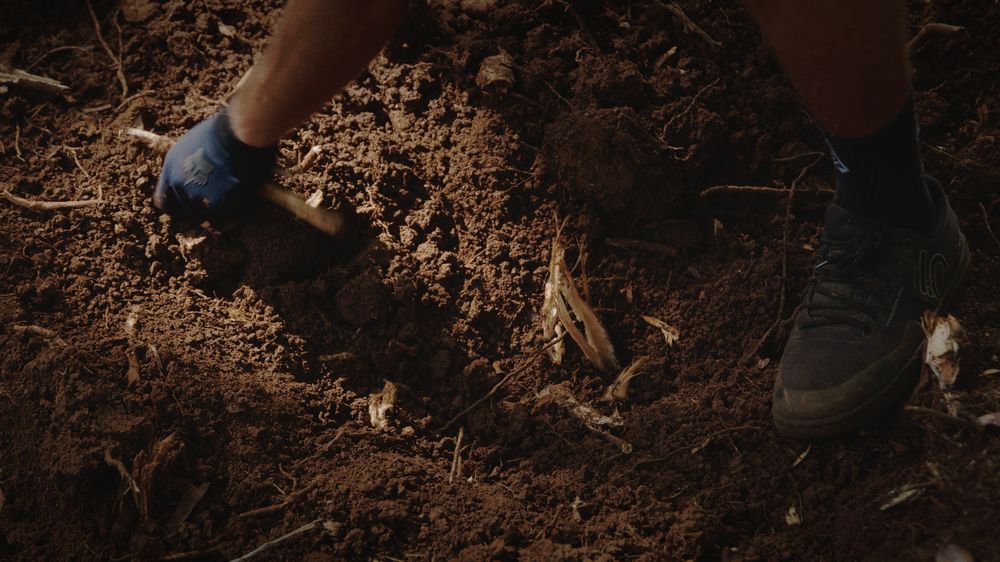 Gloved hands and a shoe in the dirt while packing the berm