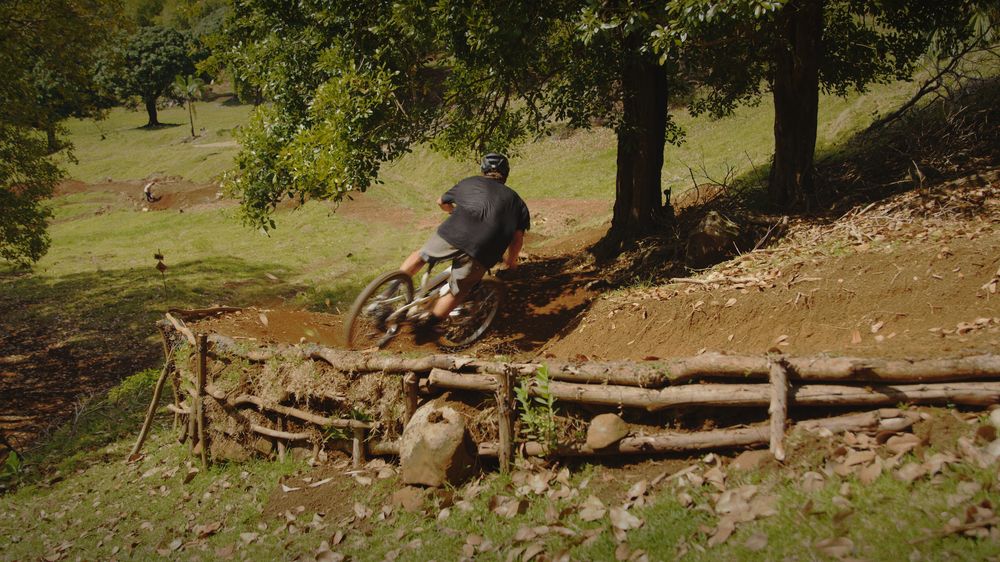 A rider leans into the freshly built right berm, log retaining wall in front
