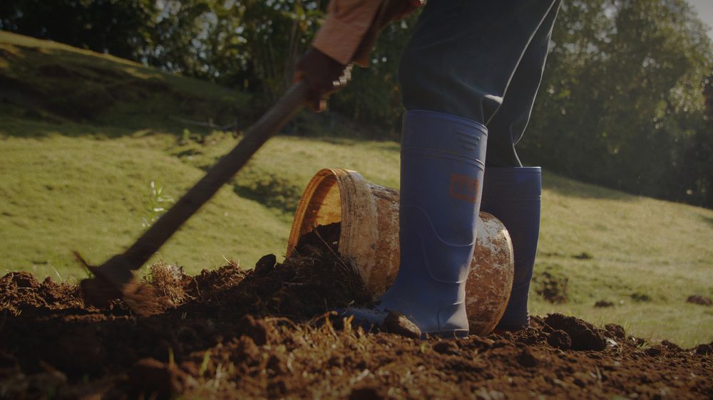 Blue rubber boots and a spade turning red earth