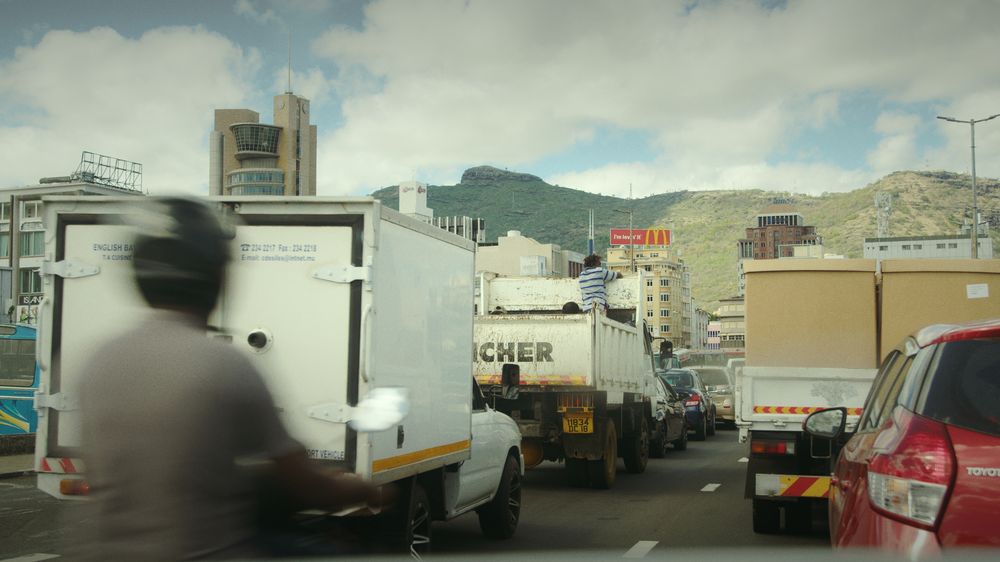 Trucks and a motorbike in Port Louis traffic with the mountains behind the city