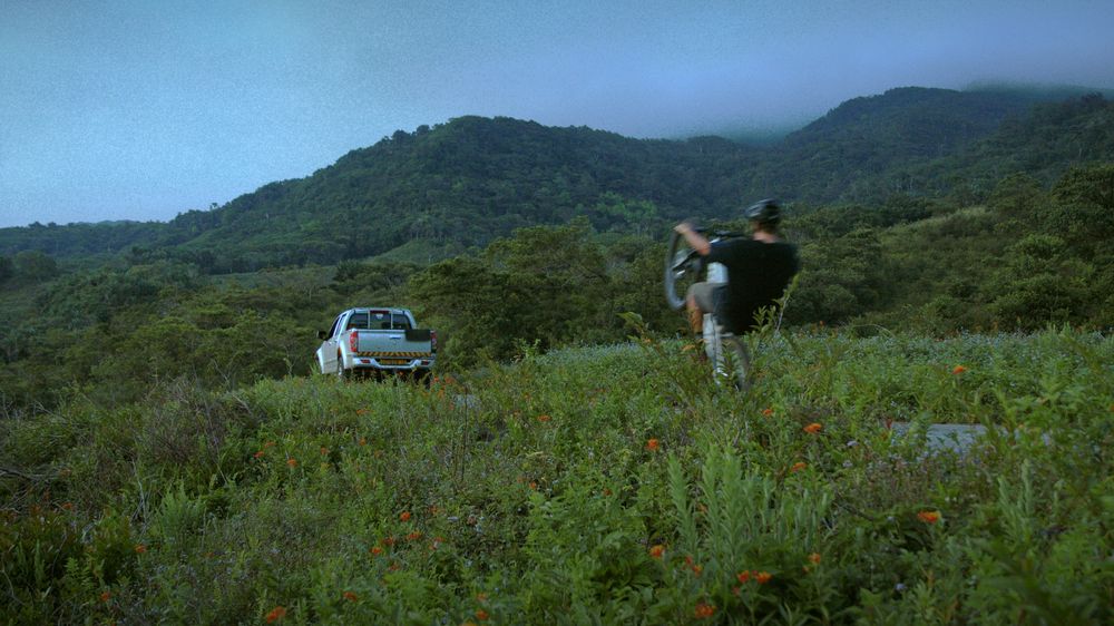 A rider walks away from the truck into green hills under low cloud