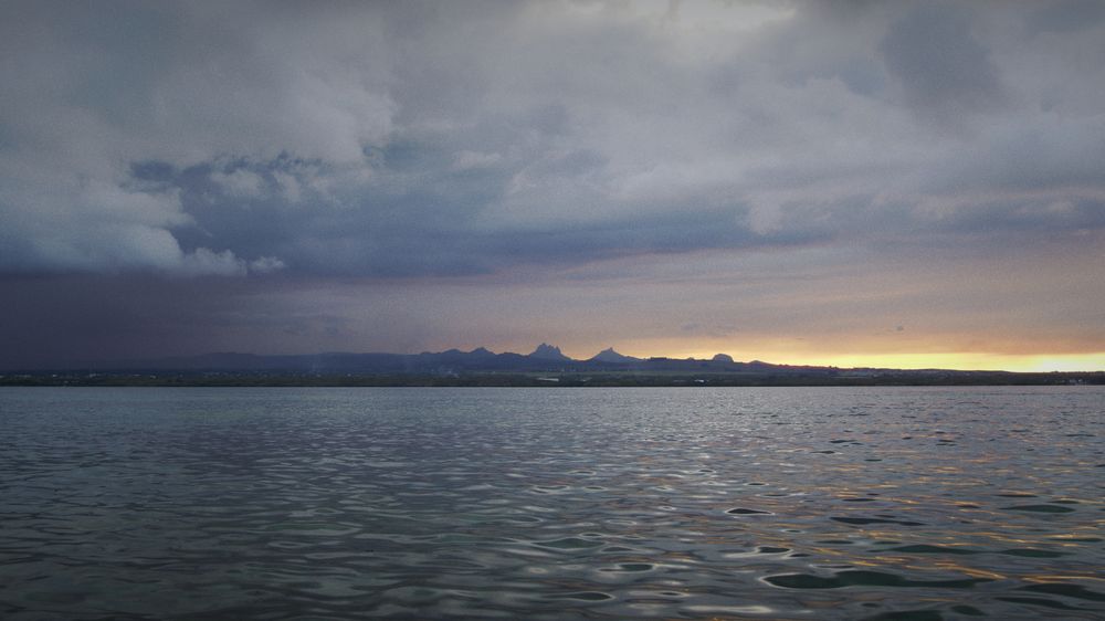 A calm sea at dusk with mountains on the horizon
