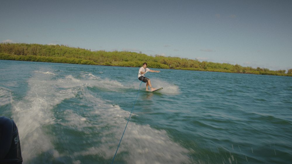 A wakeboarder carves across the lagoon behind the boat