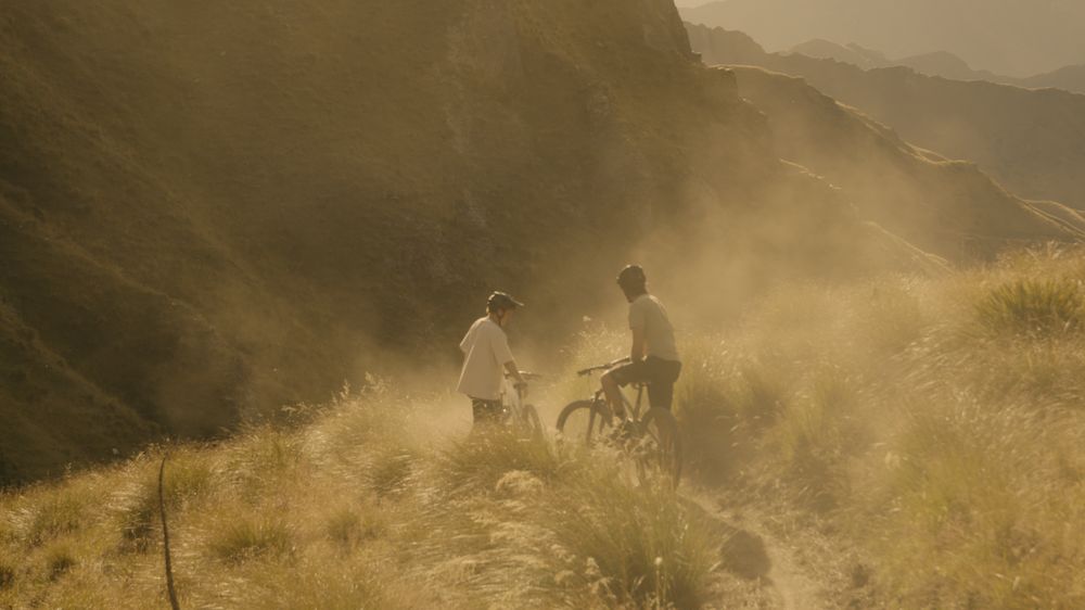 Two riders push through golden dust on a canyon trail
