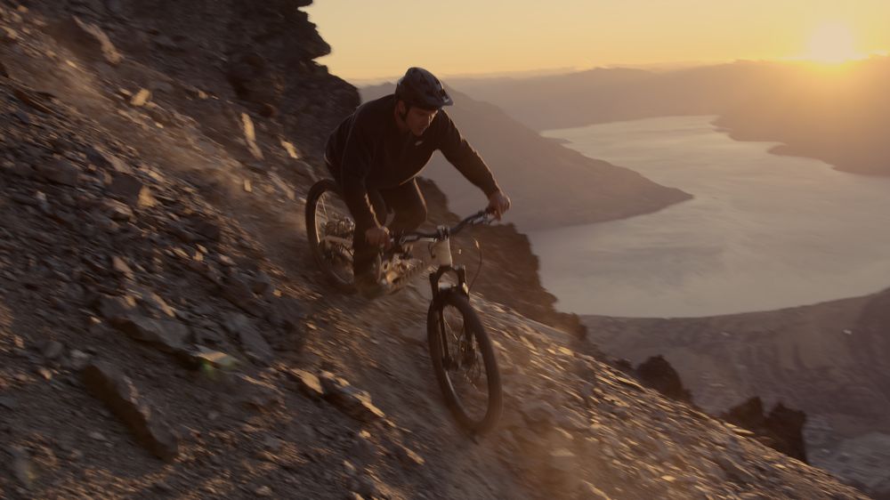 A rider drops down a rocky ridge at sunset, the lake far below