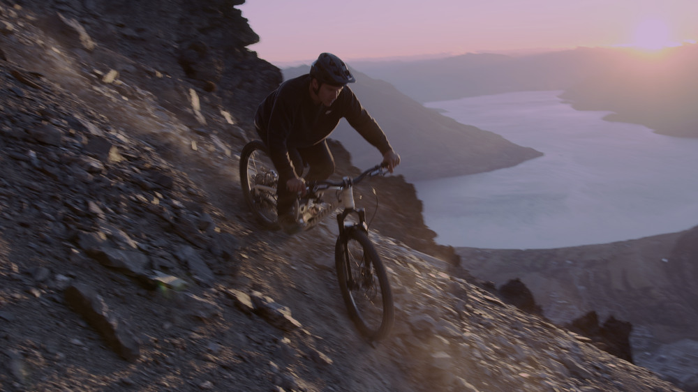 A rider drops down a rocky ridge at sunset, the lake far below